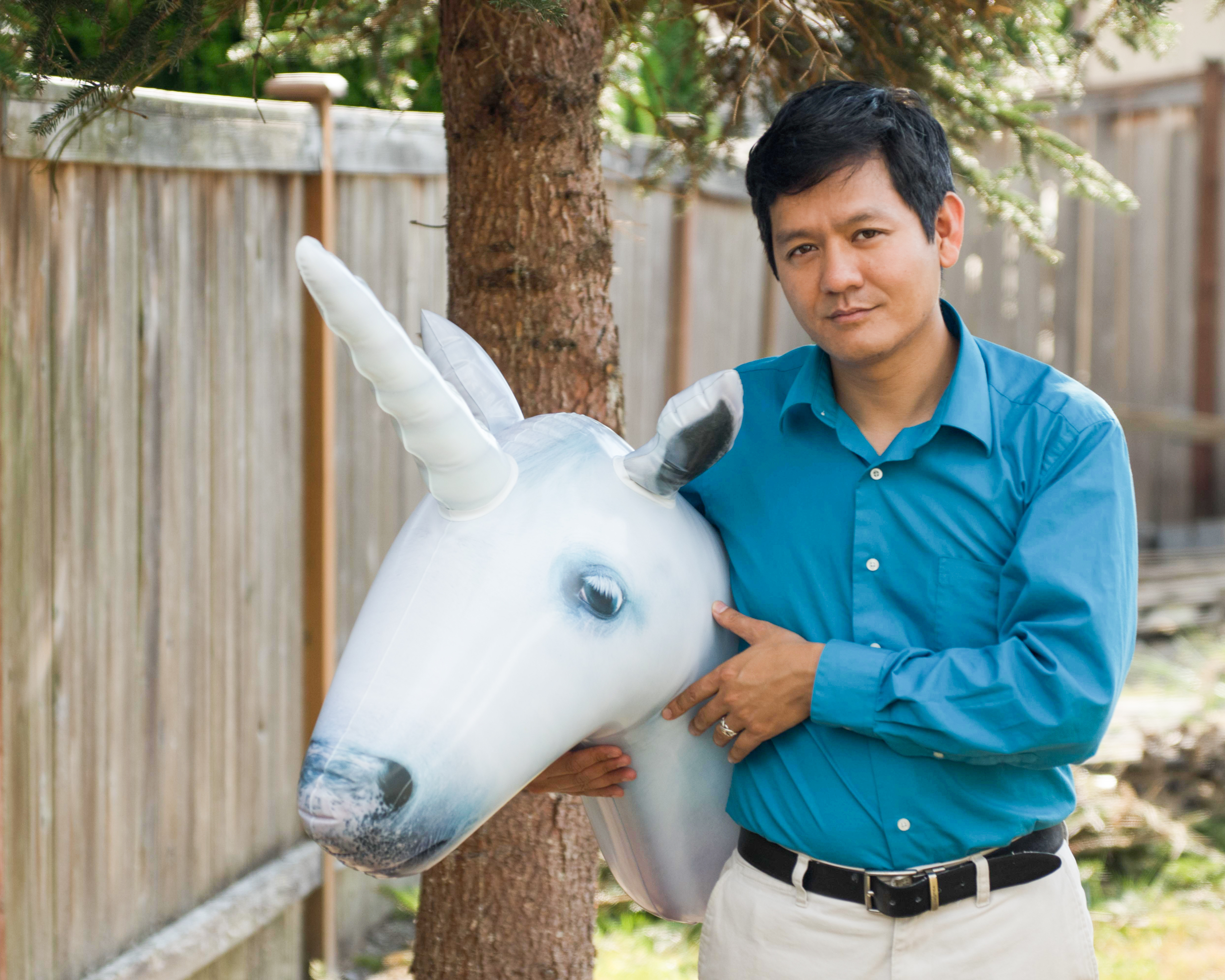 outdoor photo of man holding large unicorn stuffed animal